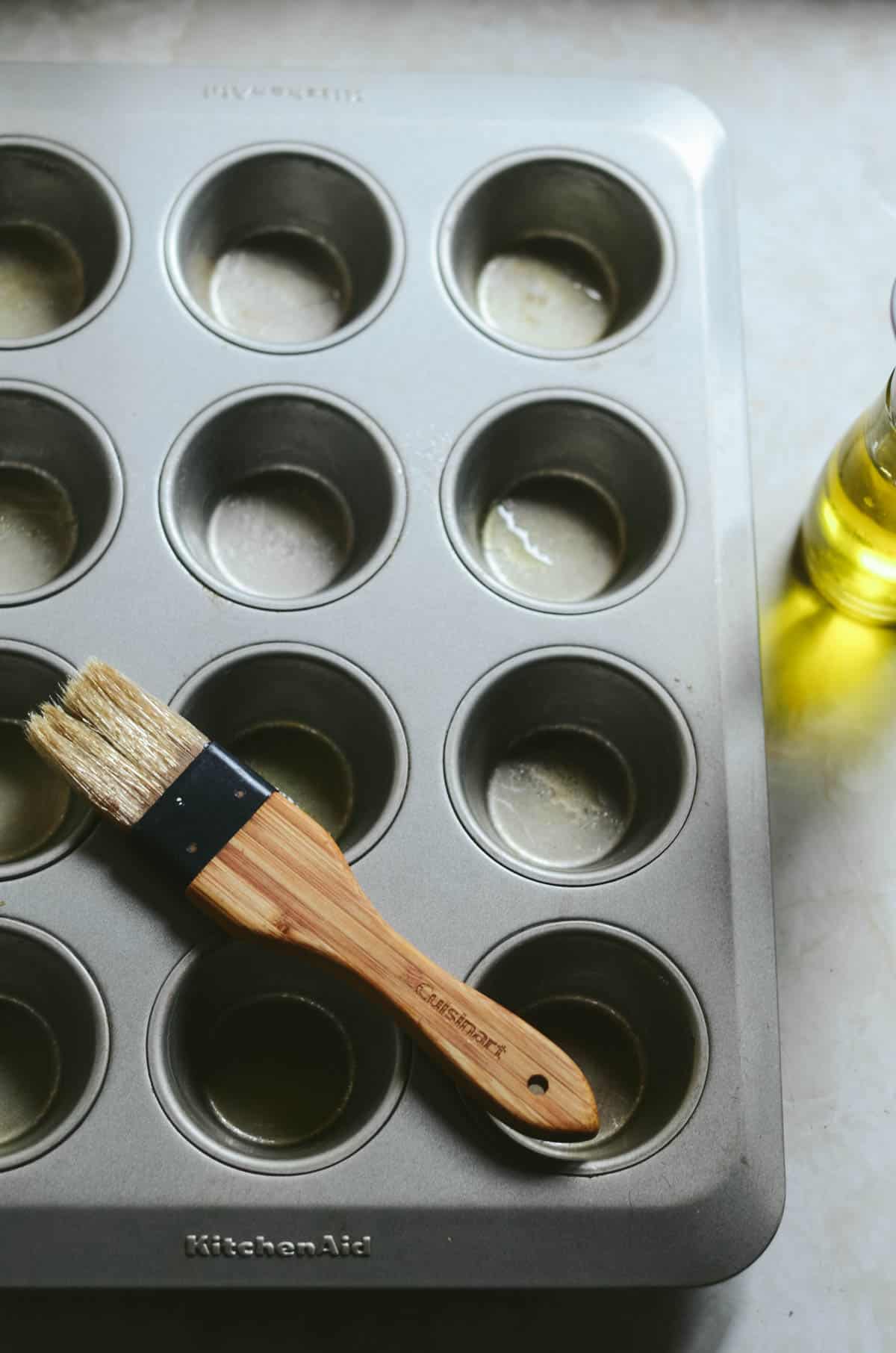 Muffins tray being greased with a pastry brush and oil.