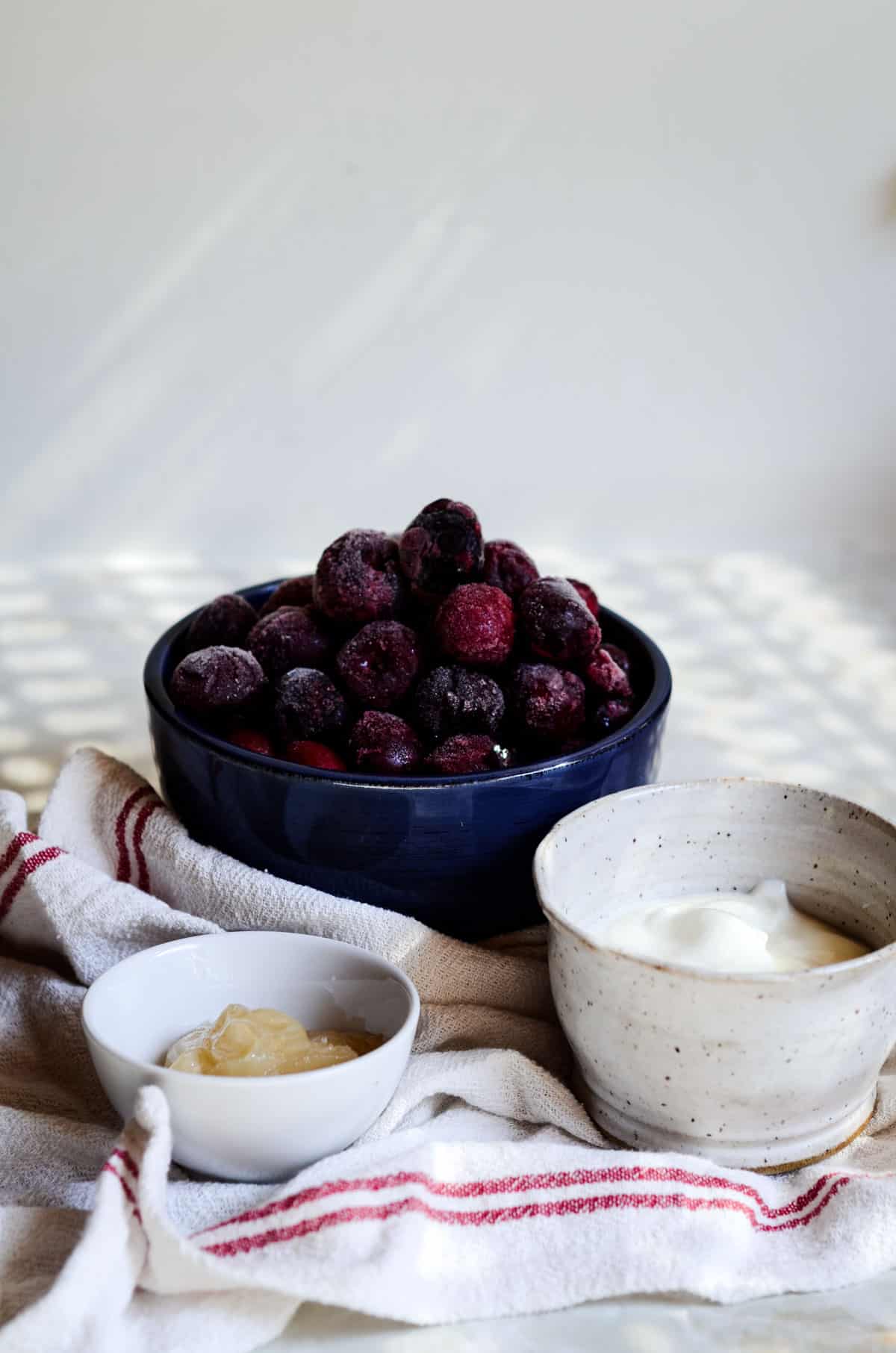 Frozen cherries, yogurt, and honey in bowls for cherry popsicles.