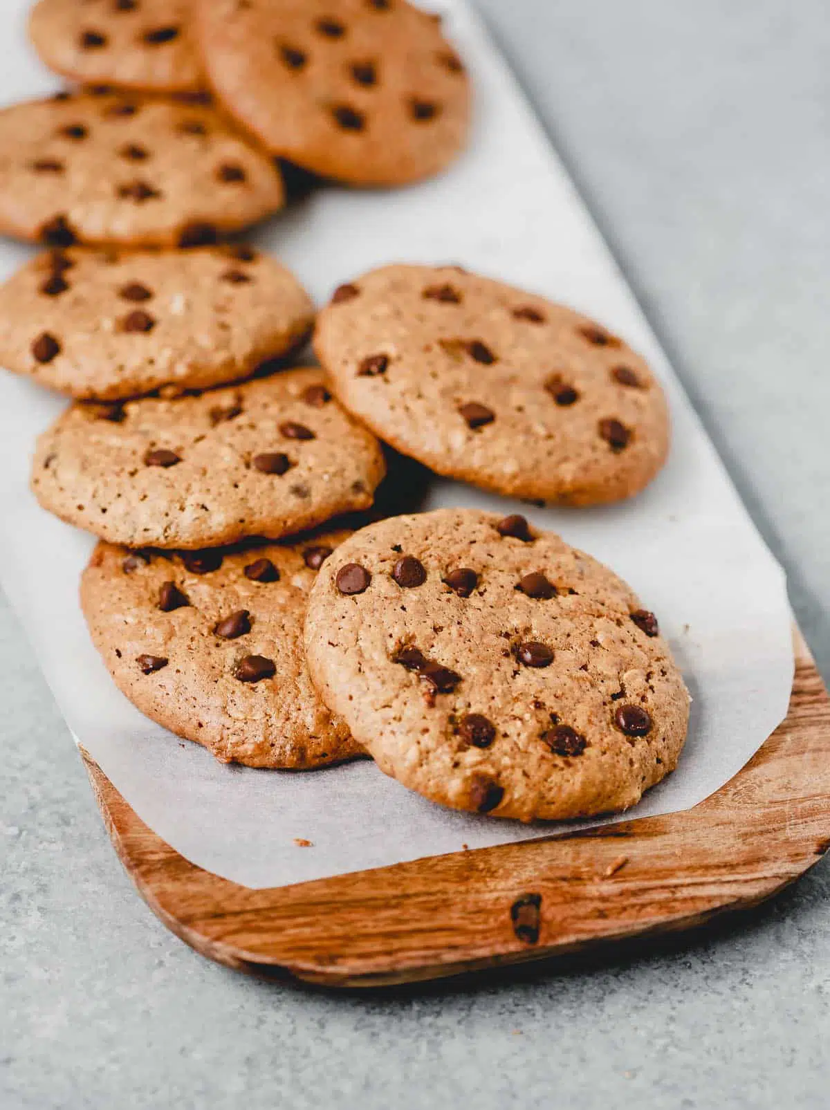 Brown cookies with oats and chocolate chips in them sitting on a wood platter.