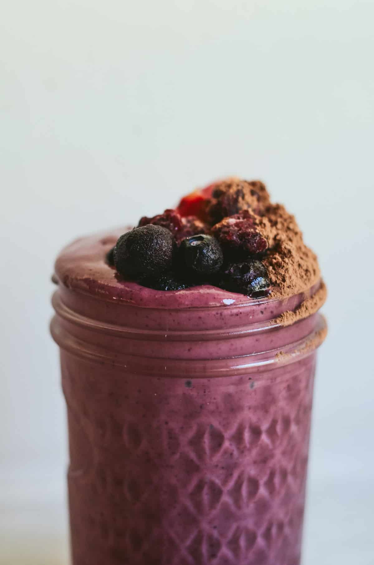 A dark purple smoothie with blueberries, strawberries, blackberries, cocoa powder on top.
