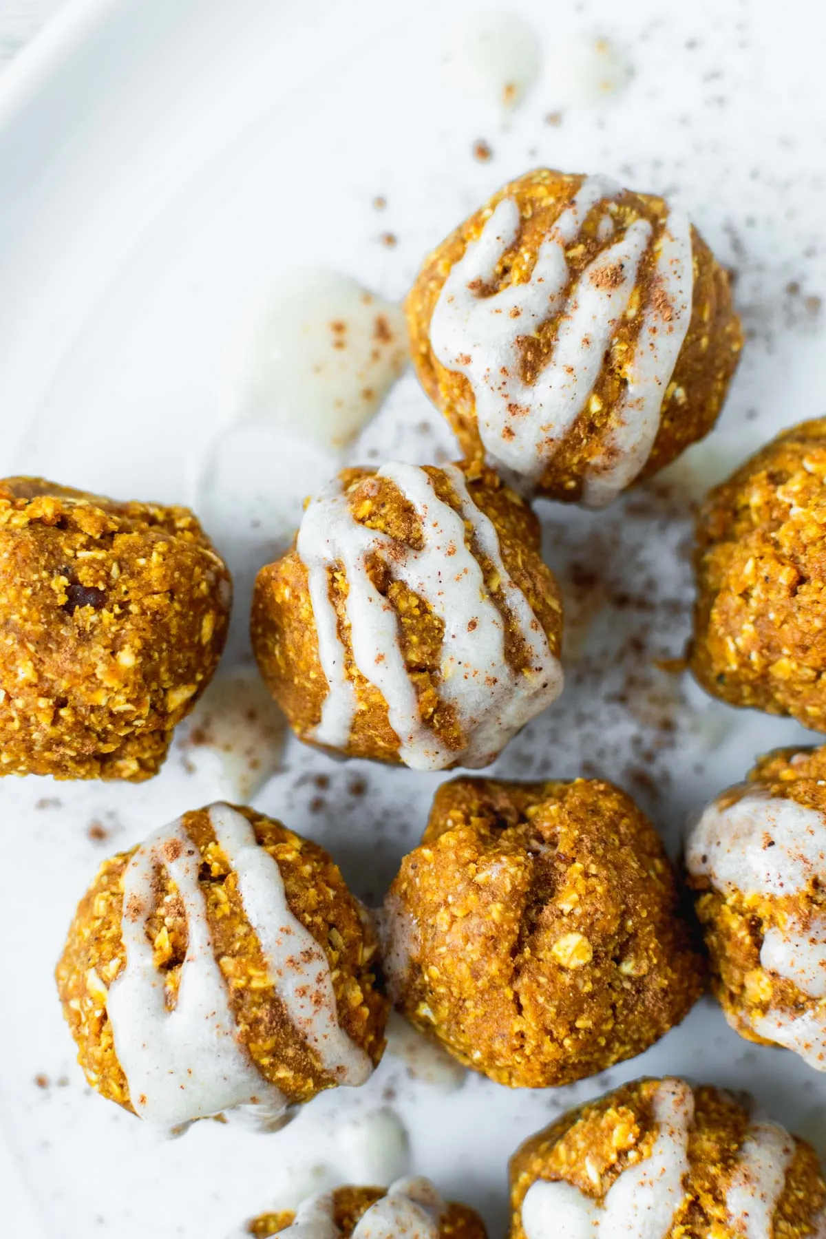 Pumpkin colored energy balls with white icing drizzled on top, siting on a white plate.