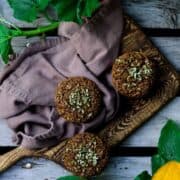 A flat lay image of brown bran zucchini muffins on a serving platter with a zucchini plant and flower beside it.