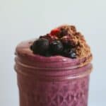 A dark purple smoothie with blueberries, strawberries, blackberries, cocoa powder on top.