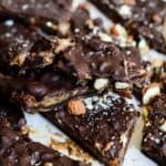Rough pieces of chocolate covered dates and nuts on white parchment paper.