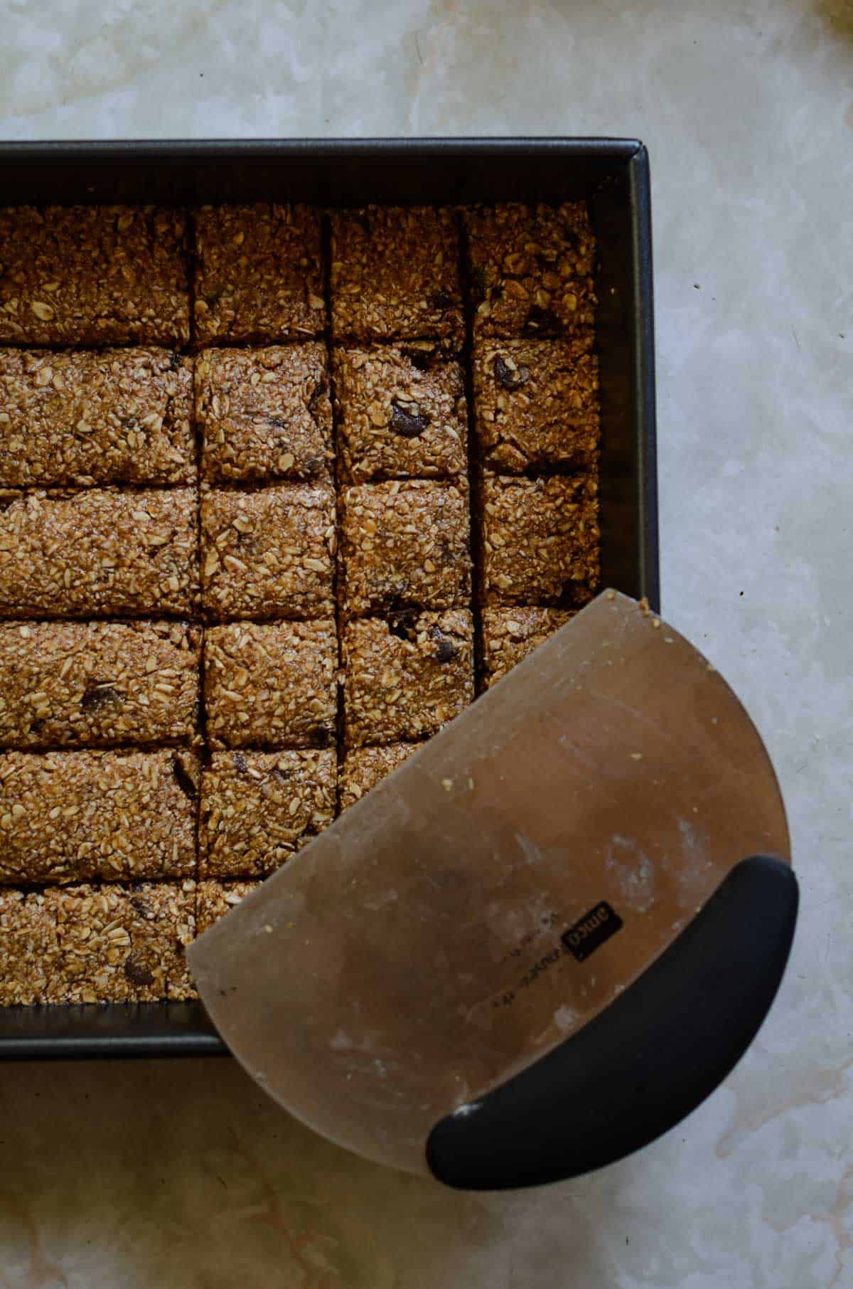 Oatmeal chocolate chip batter pressed into an 8x8 pan being cut into little squares with a pastry cutter.