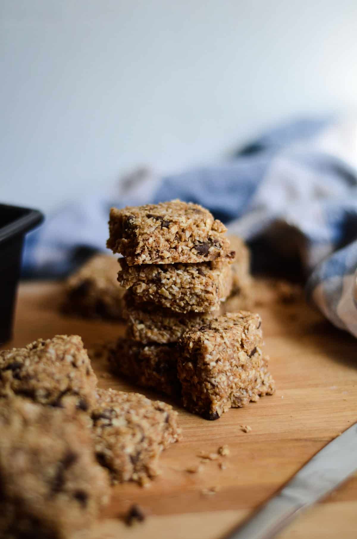 Oatmeal chunks with chocolate chips stacked on top on each other with a knife and a baking pan and tea towel beside.