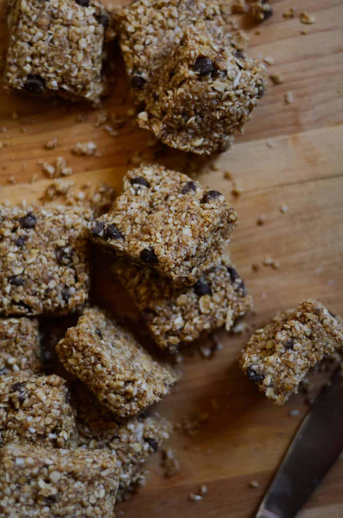 Little oatmeal chunks with chocolate chips scattered on a wooden cutting board.