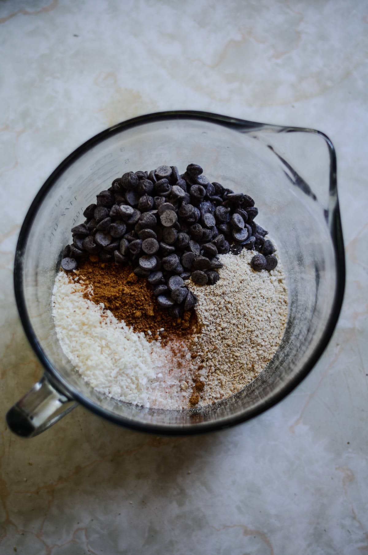 Chocolate chips, coconut sugar, oats, ground oats in a glass mixing bowl.