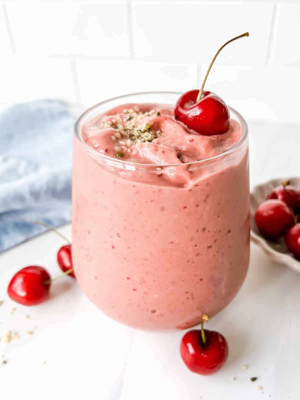 Pink smoothie in glass cup with cherries on top.