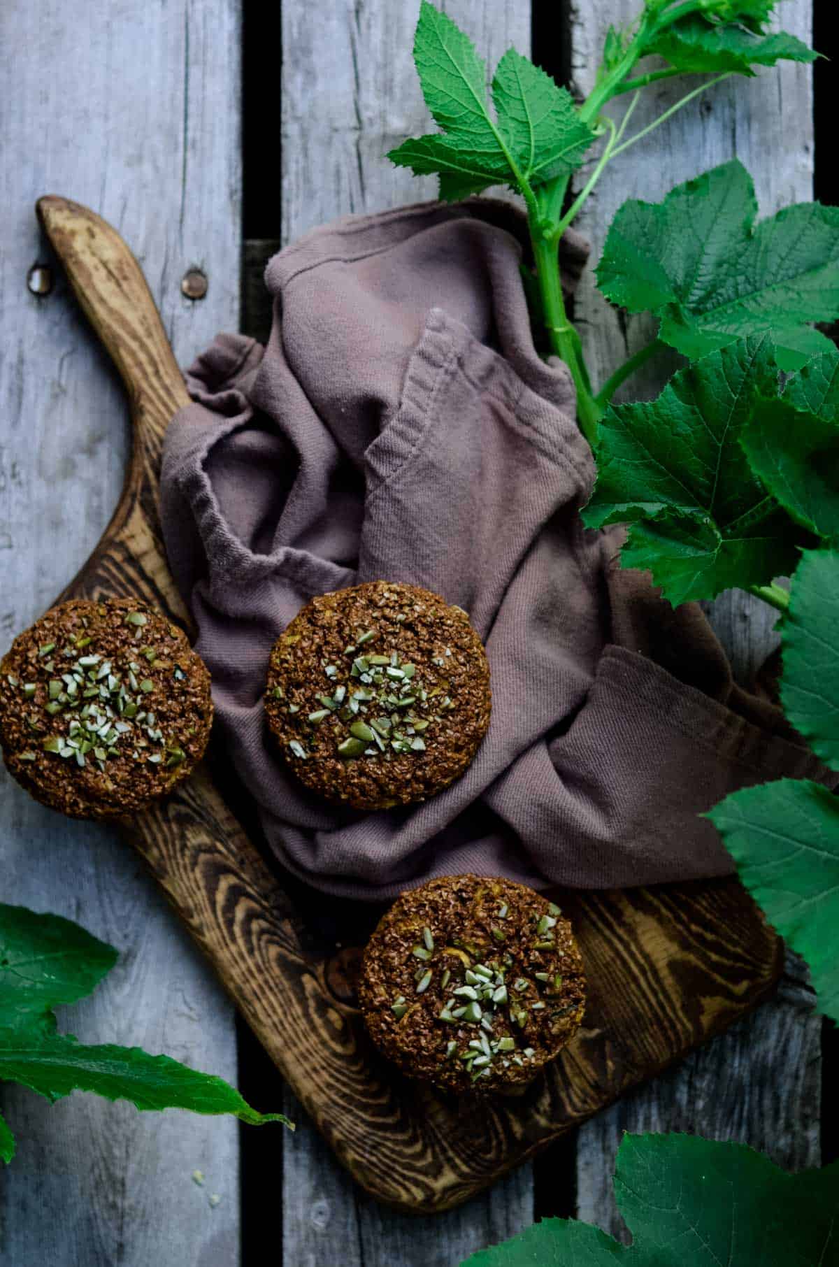 Zucchini Bran Muffins on a wooden serving board surrounded by green zucchini leaves of the plant.