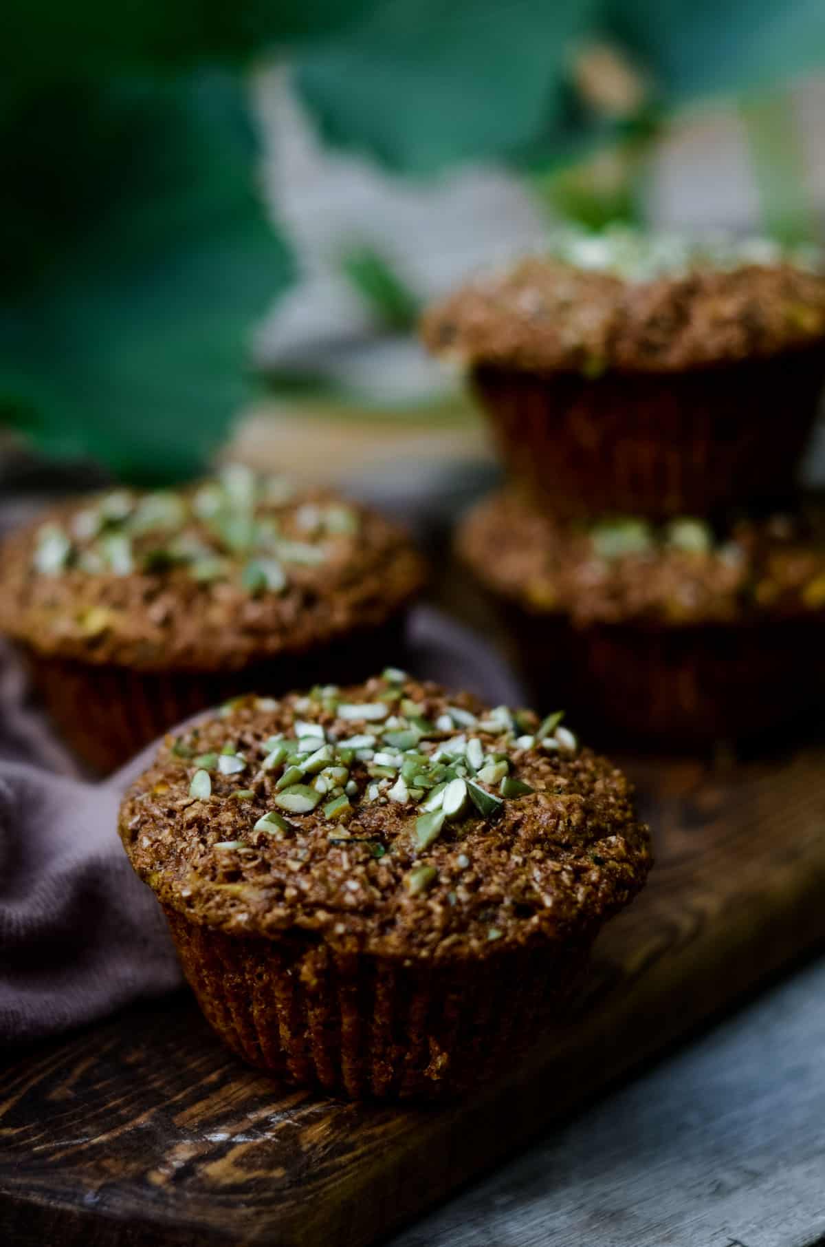 Brown bran zucchini muffins with chopped green pumpkin seeds on top, on a wooden serving platter.