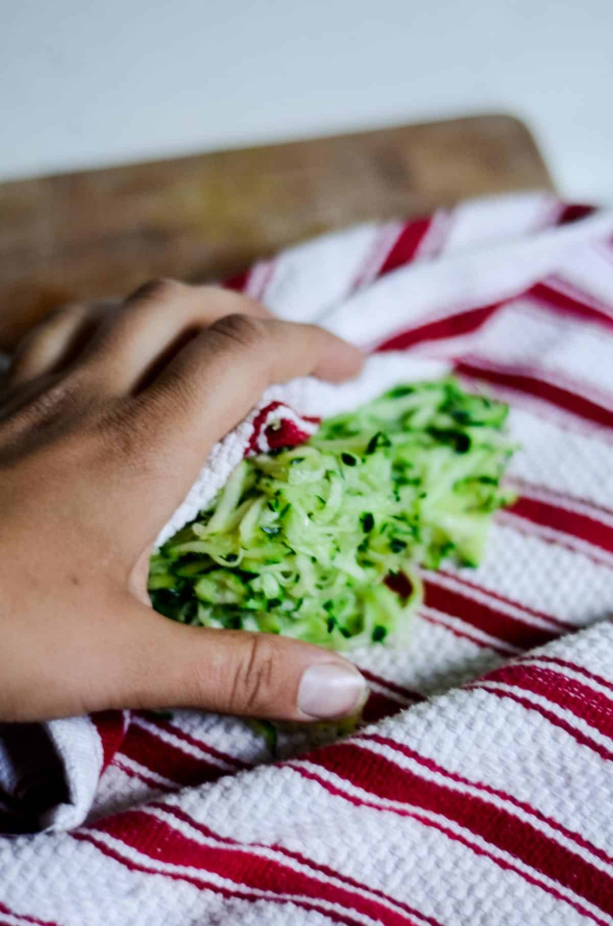 Grated zucchini in a dish towel, hand squeezing out the moisture. 