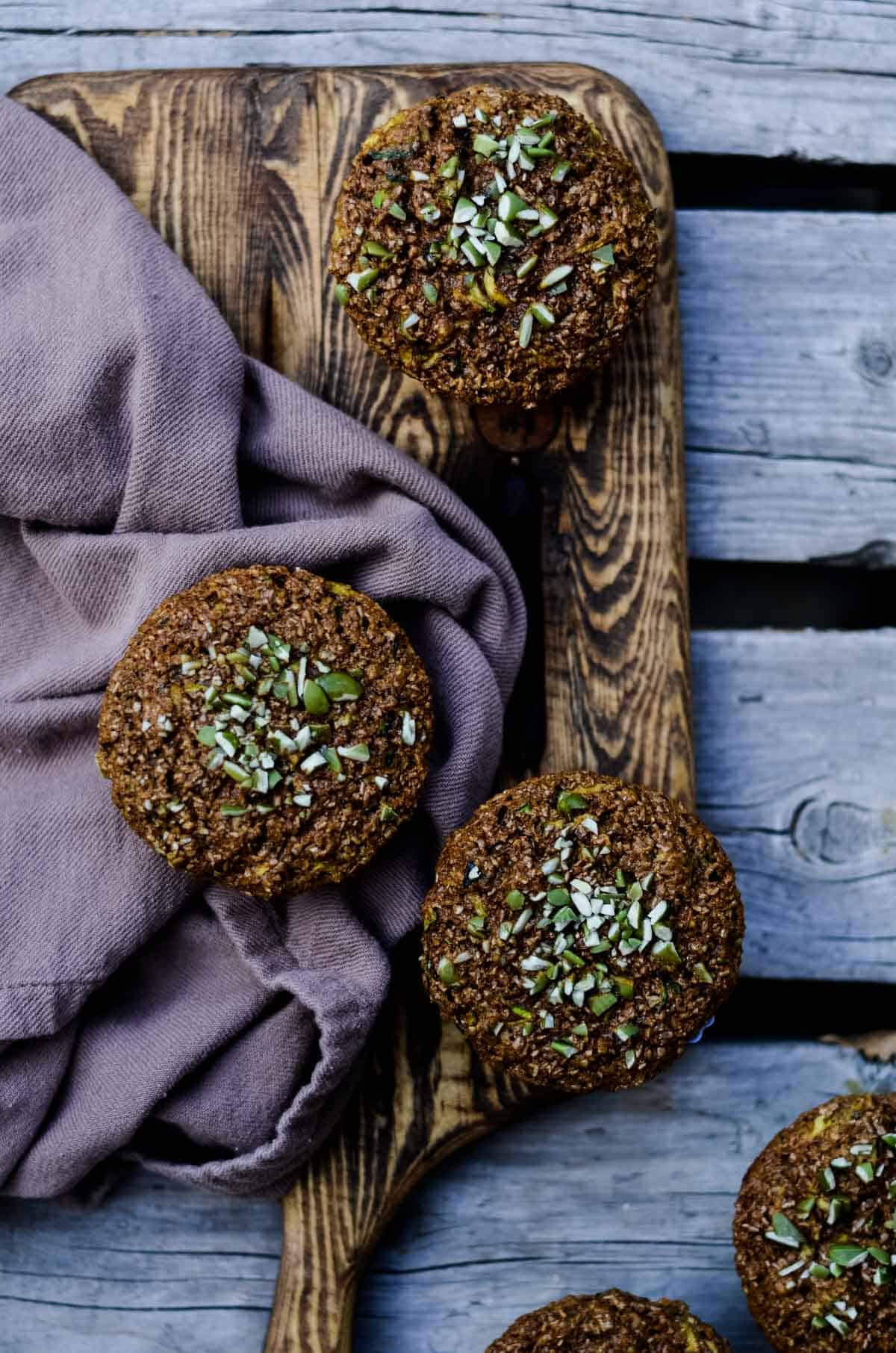 Brown muffins with chopped pumpkin seeds on top sitting on a cutting board.
