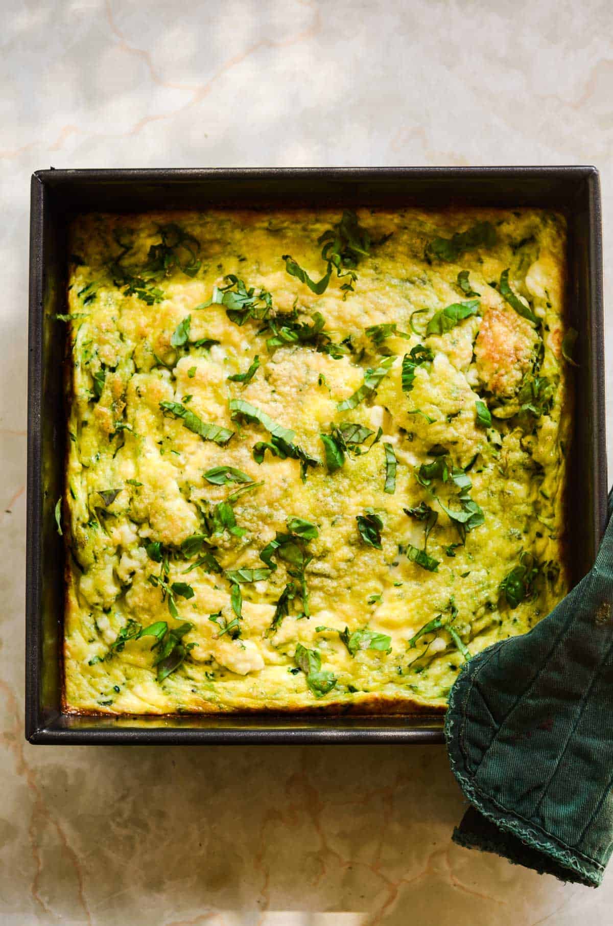 Flay lay of yellow eggs baked with green flecks of zucchini and fresh basil.