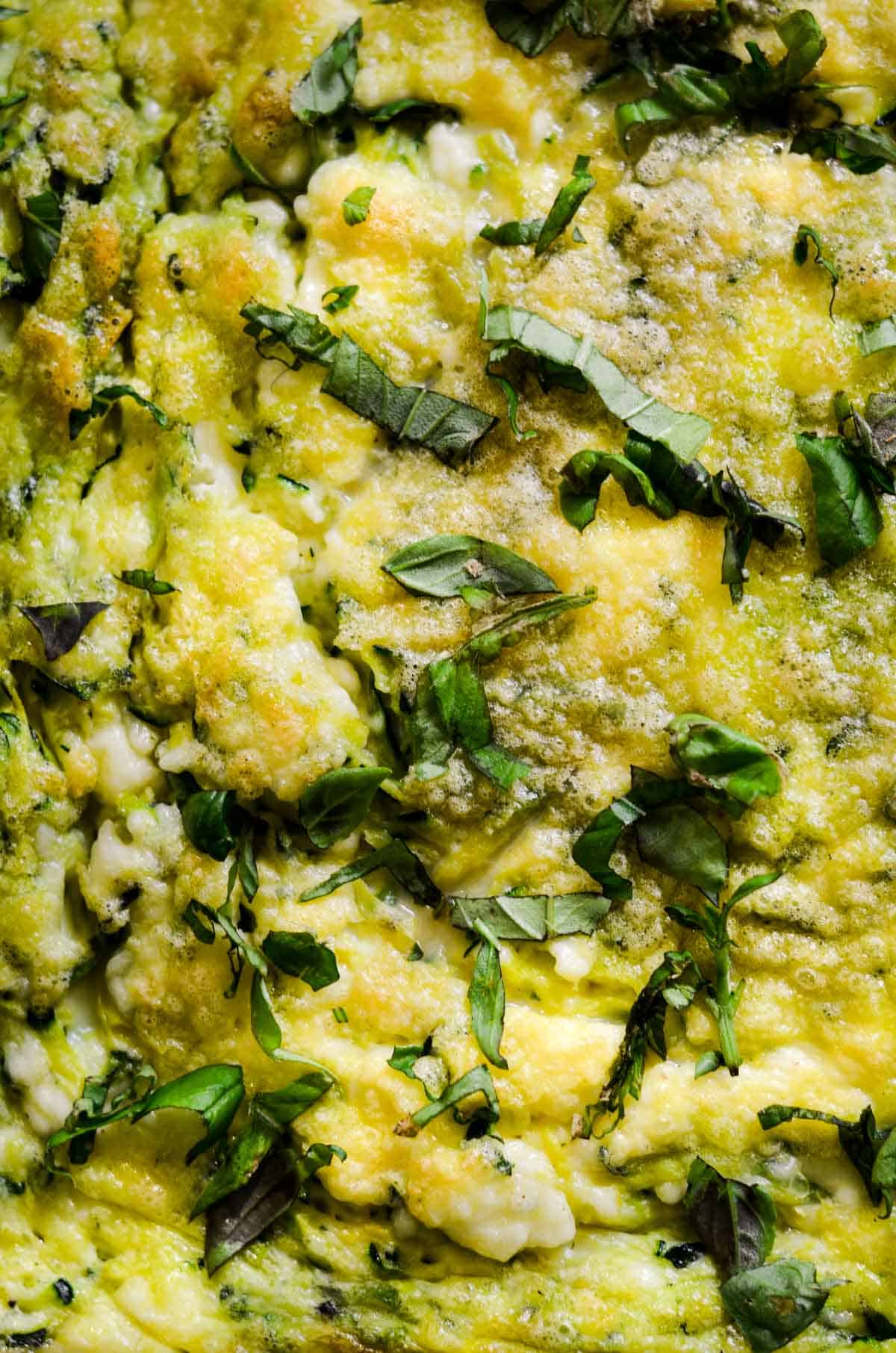 Close up of baked eggs, with green zucchini flecks, and chopped basil on top.