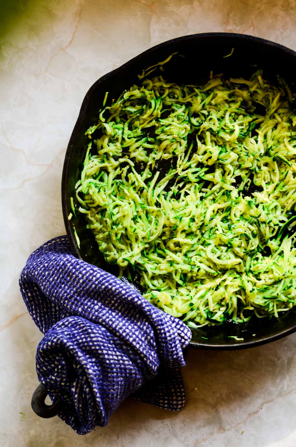 Shredded zucchini in a cast iron frying pan.