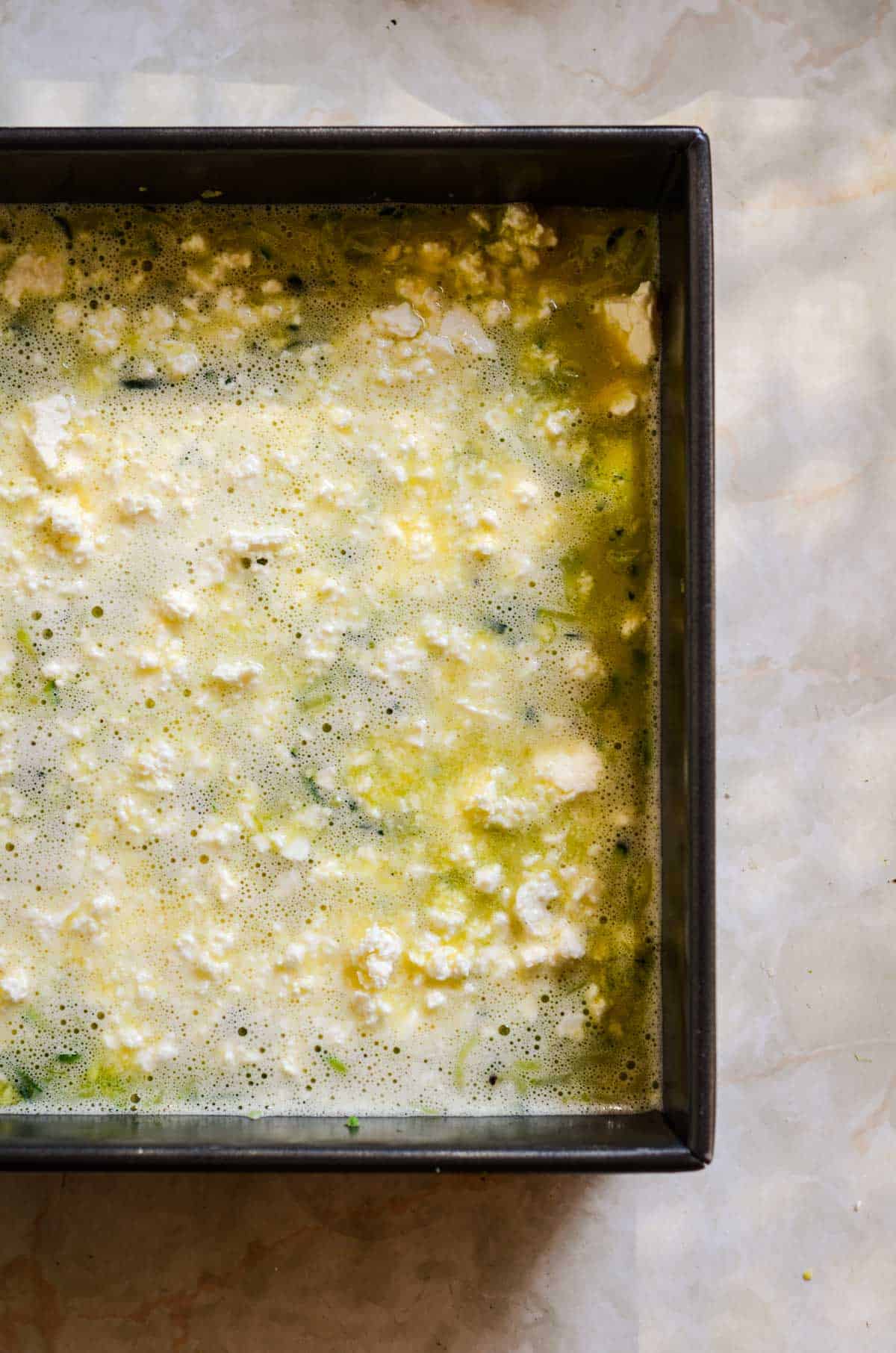Zucchini, whisked eggs, feta, in baking pan ready to be baked.