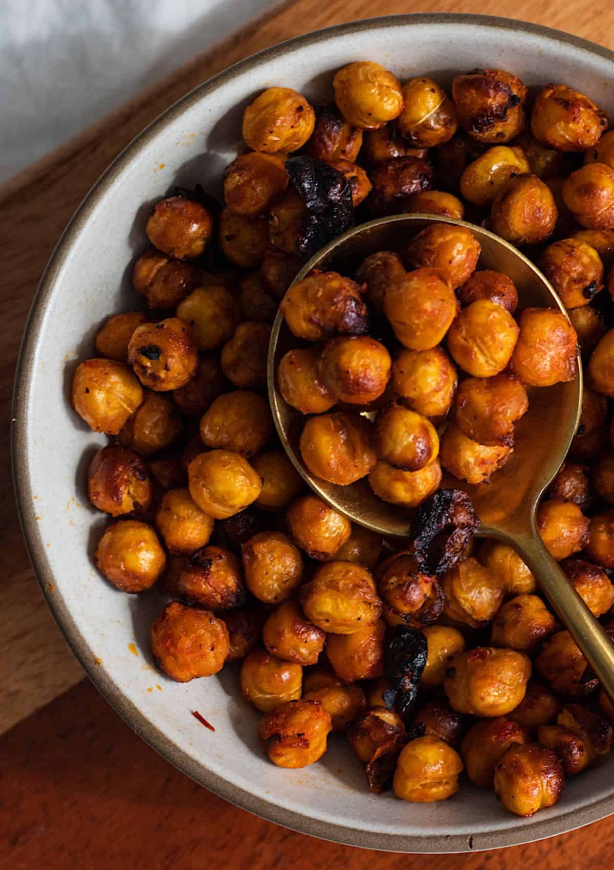 Dark orange colored chickpeas in a bowl with a spoon full of chickpeas.