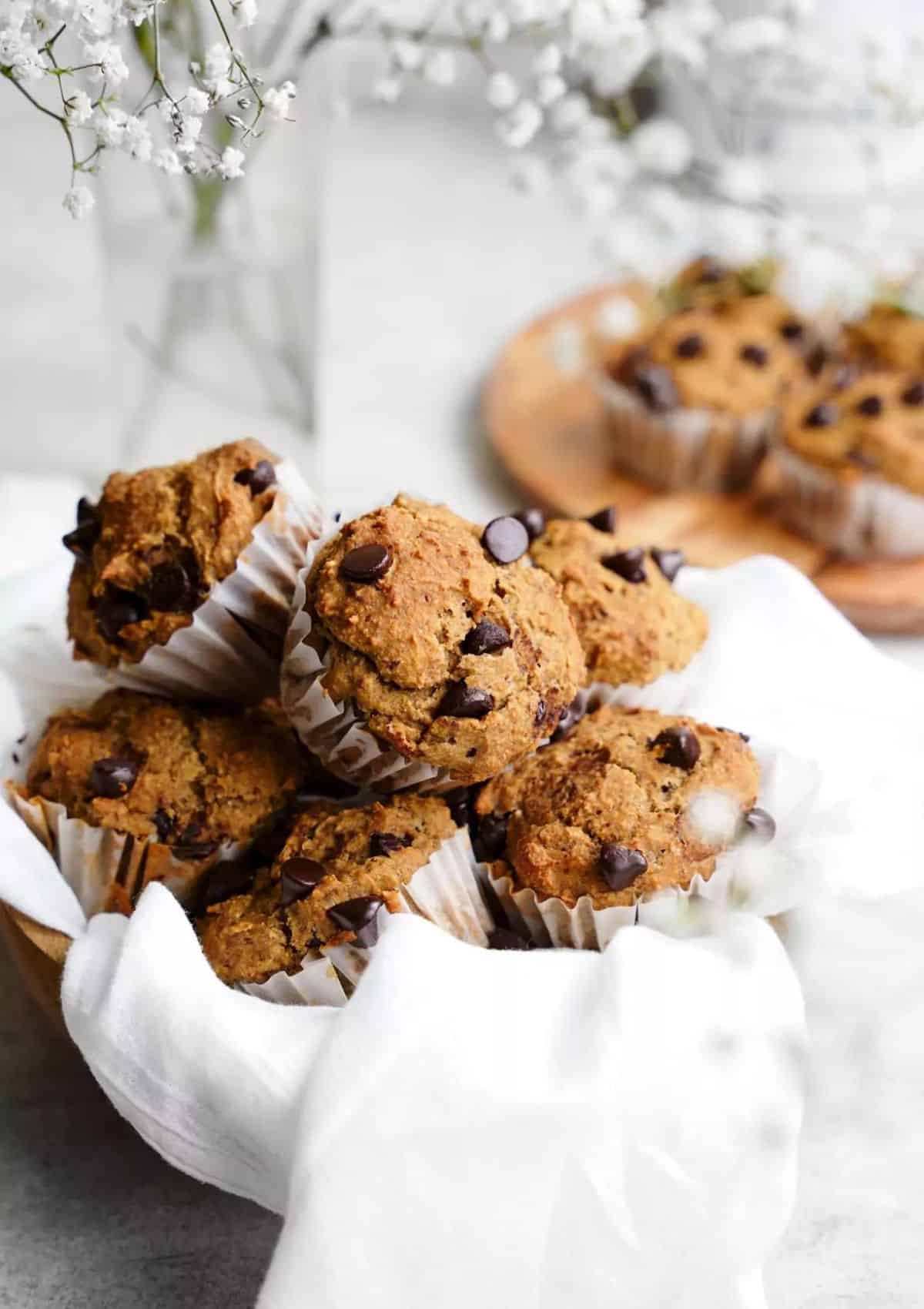 Brown muffins with chocolate chips in a bowl with a white napkin and baby's breath.