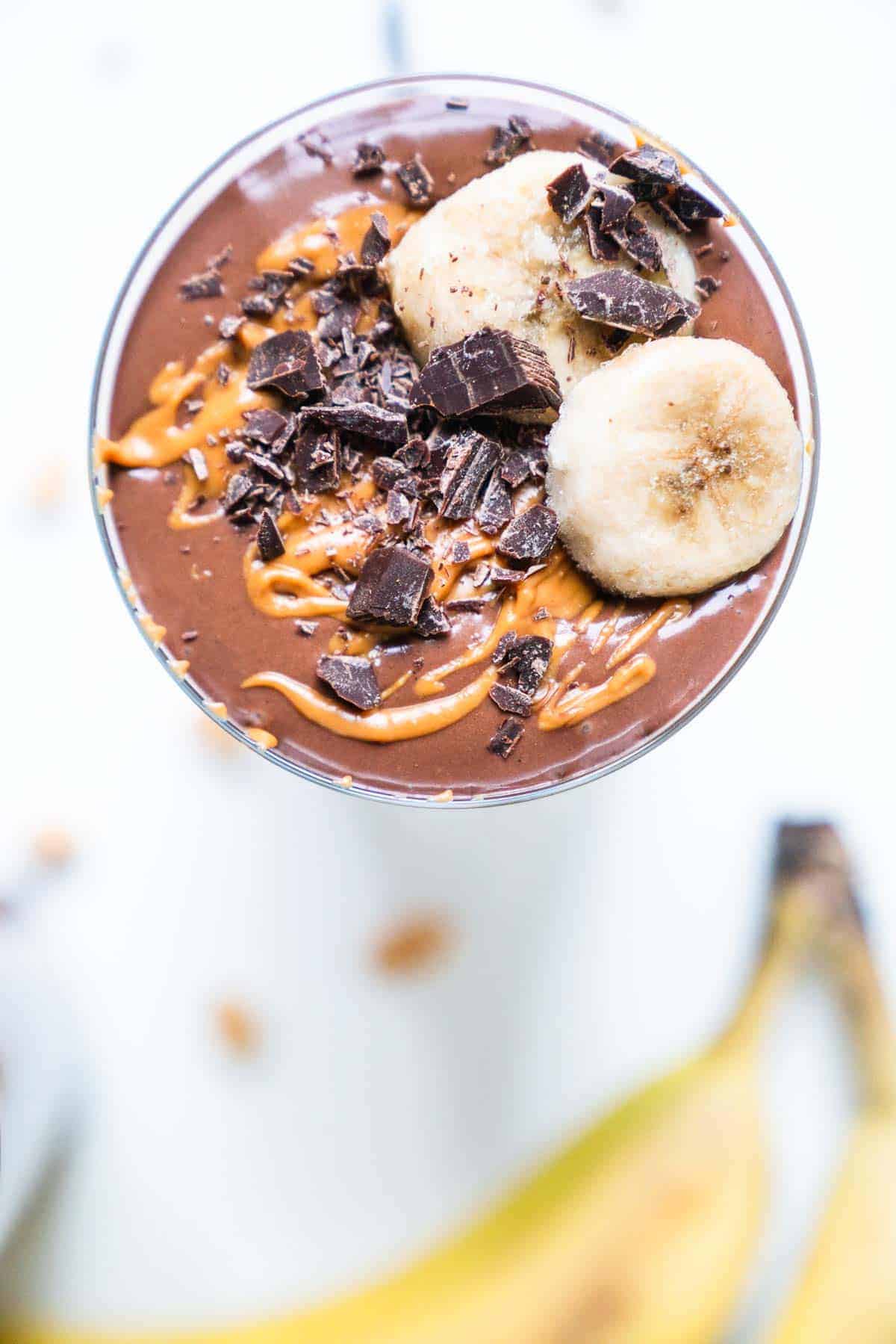 Brown smoothie in cup with peanut butter and chocolate and banana on top.