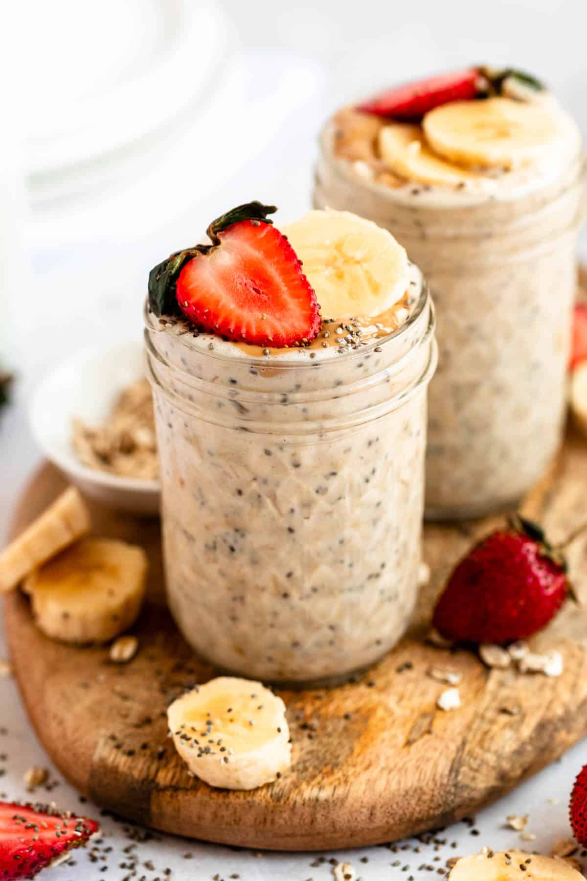 Jars filled with oatmeal with a strawberry and banana on top and banana beside the jar.