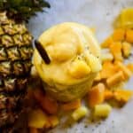 Flatlay view of a yellow tropical smoothie with a pineapple and mango beside it.