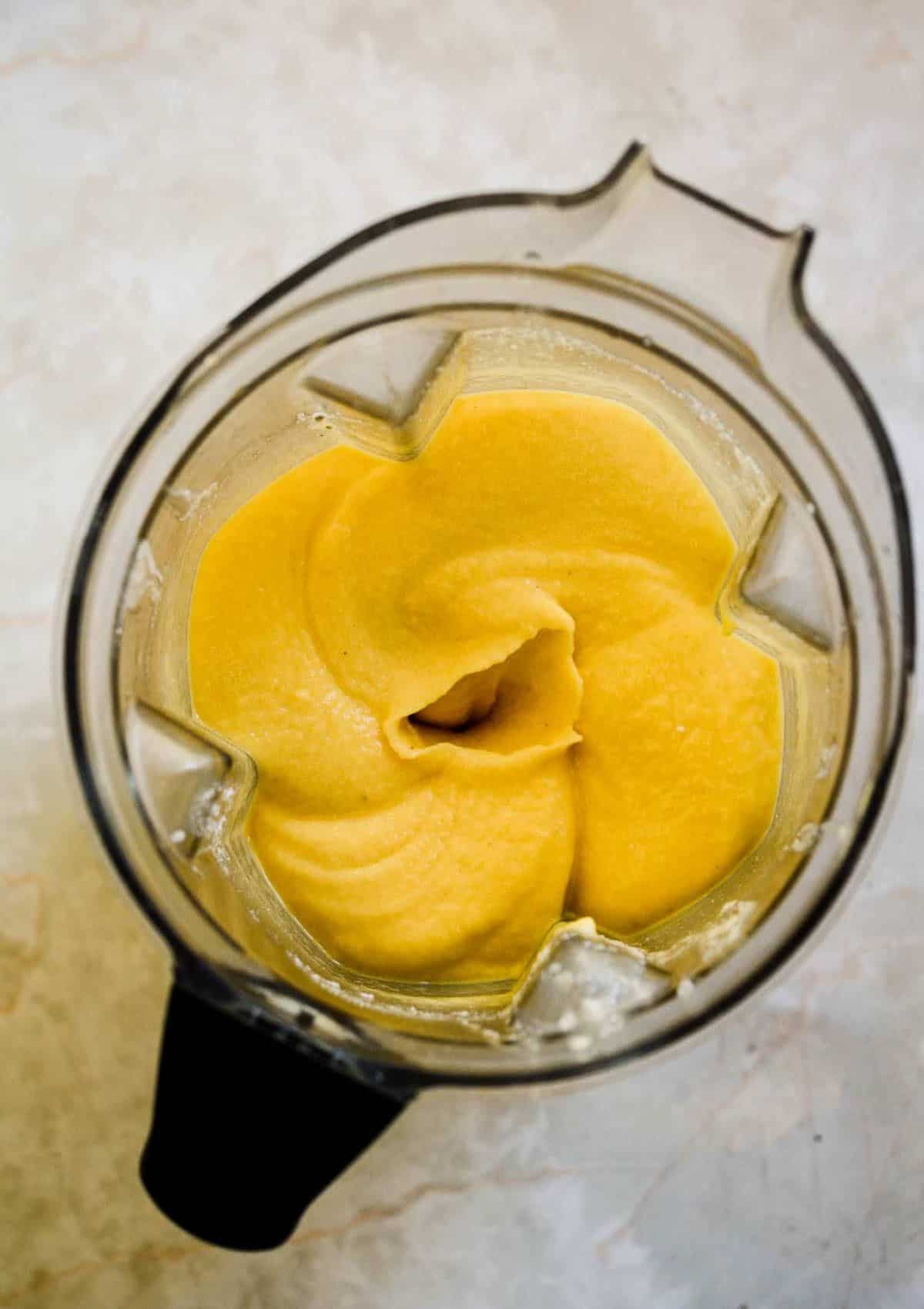 A blender container full of yellow thick smoothie.
