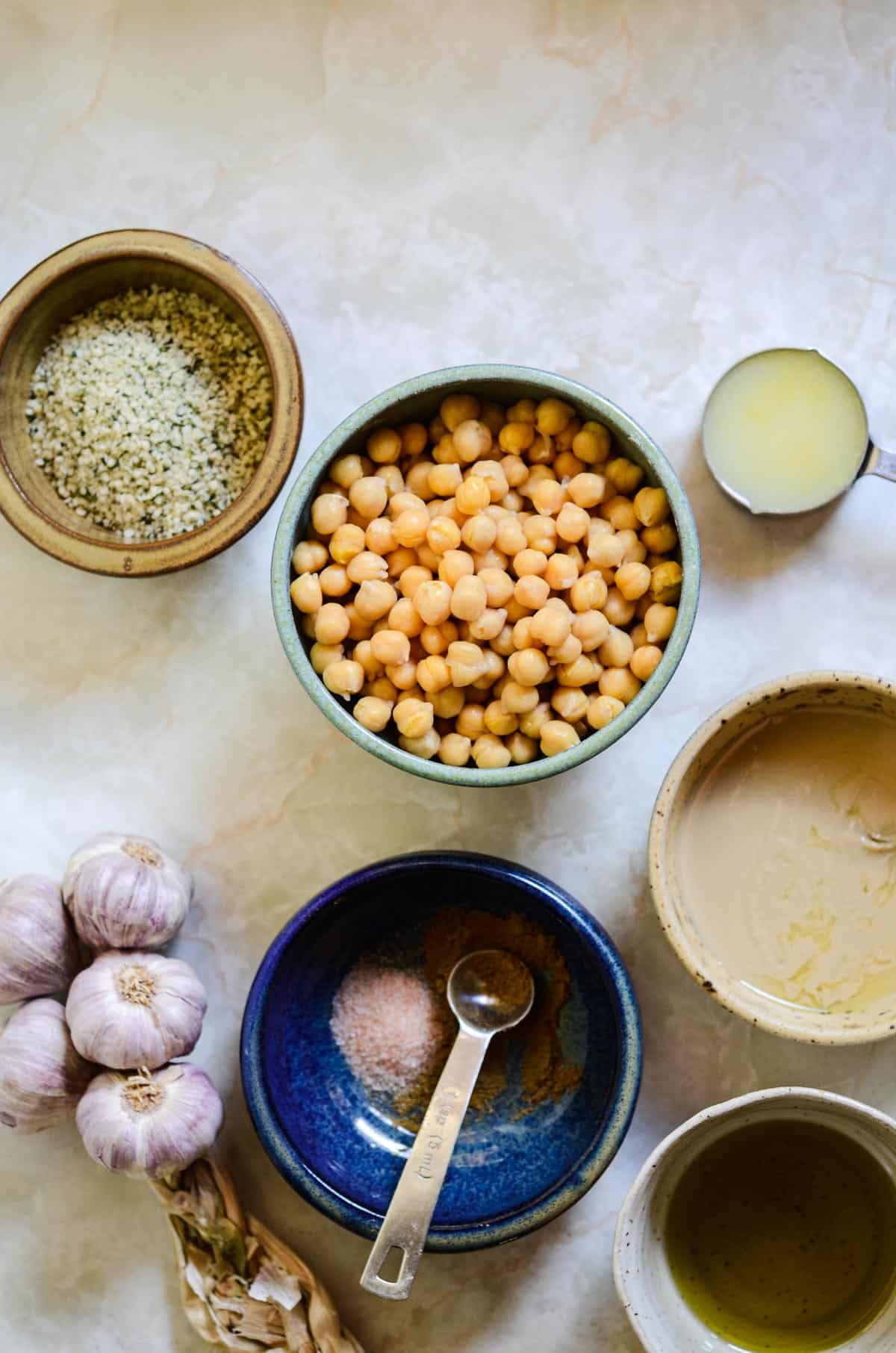 Chickpeas, lemon juice, tahini, olive oil, sea salt, cumin, garlic, and hemp hearts all measured to make hummus.