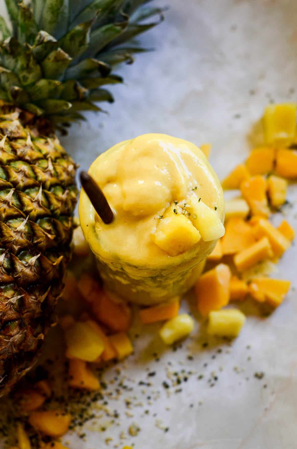 Yellow smoothie with pineapple and mango on the counter with a pineapple beside.