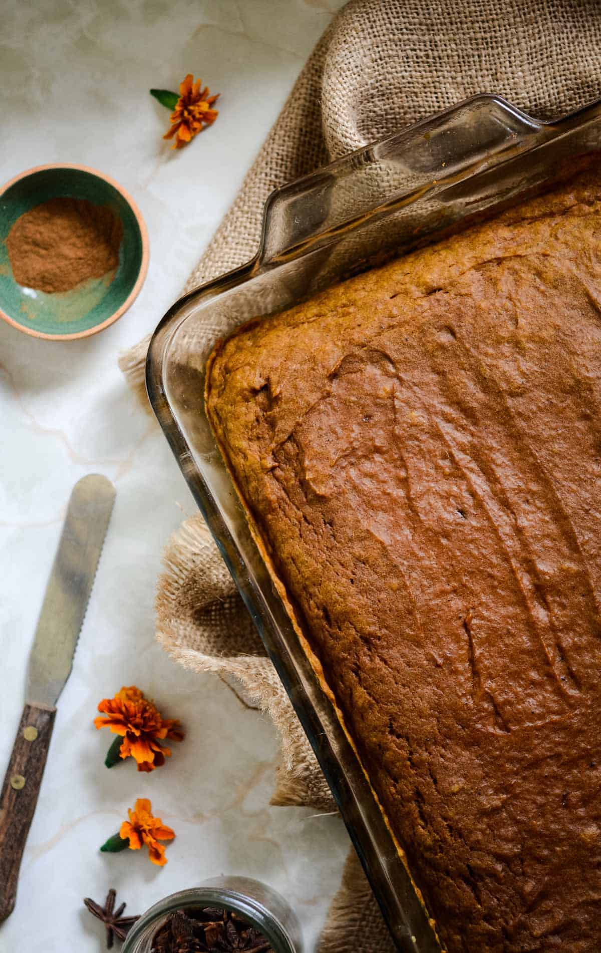 Dark orange colored sheet pan cake, with cinnamon and a knife beside.