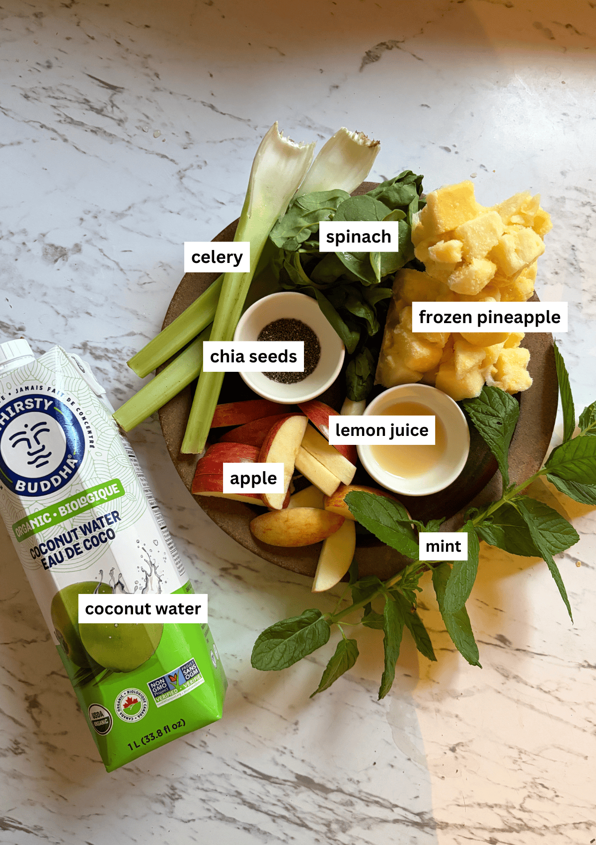 Apple, celery, mint, lemon juice, spinach. frozen pineapple on a plate, with coconut water beside it.