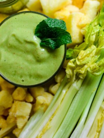 Celery stalk cut open with mango pieces beside it and a green celery smoothie.