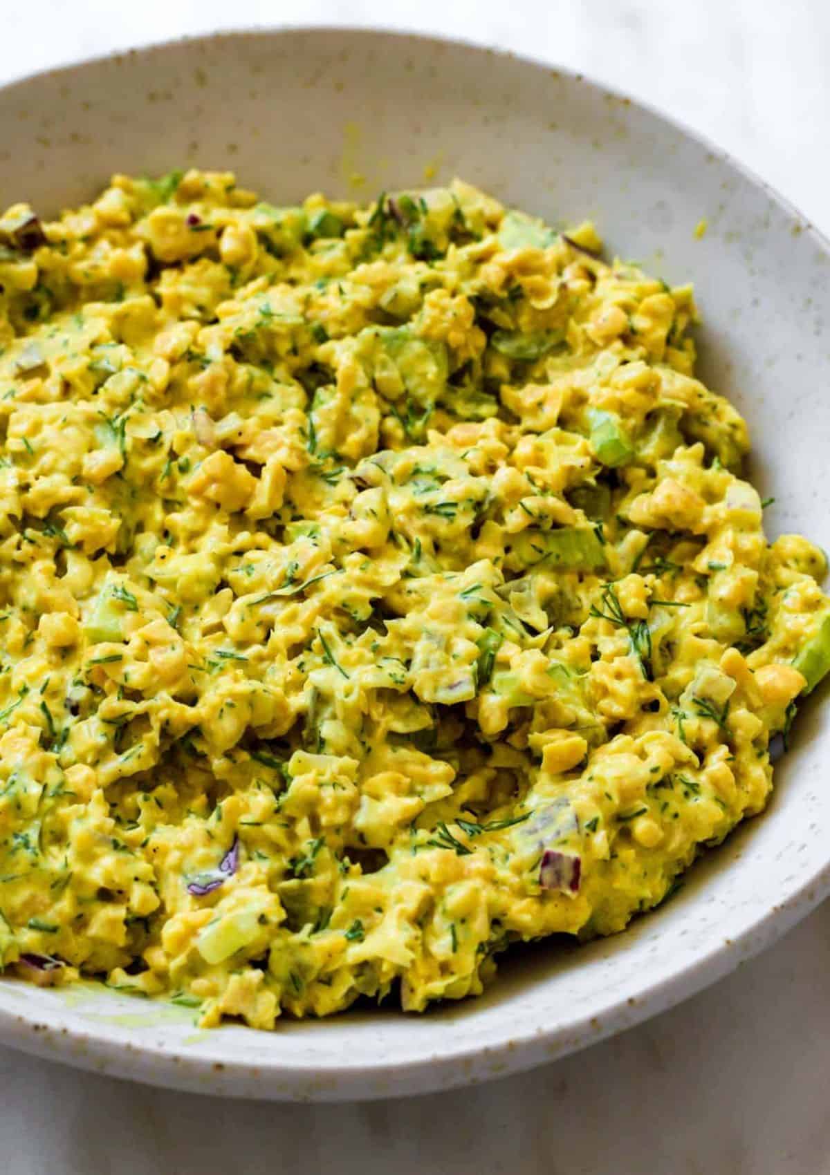 Yellow mashed chickpeas with green flecks in a bowl.