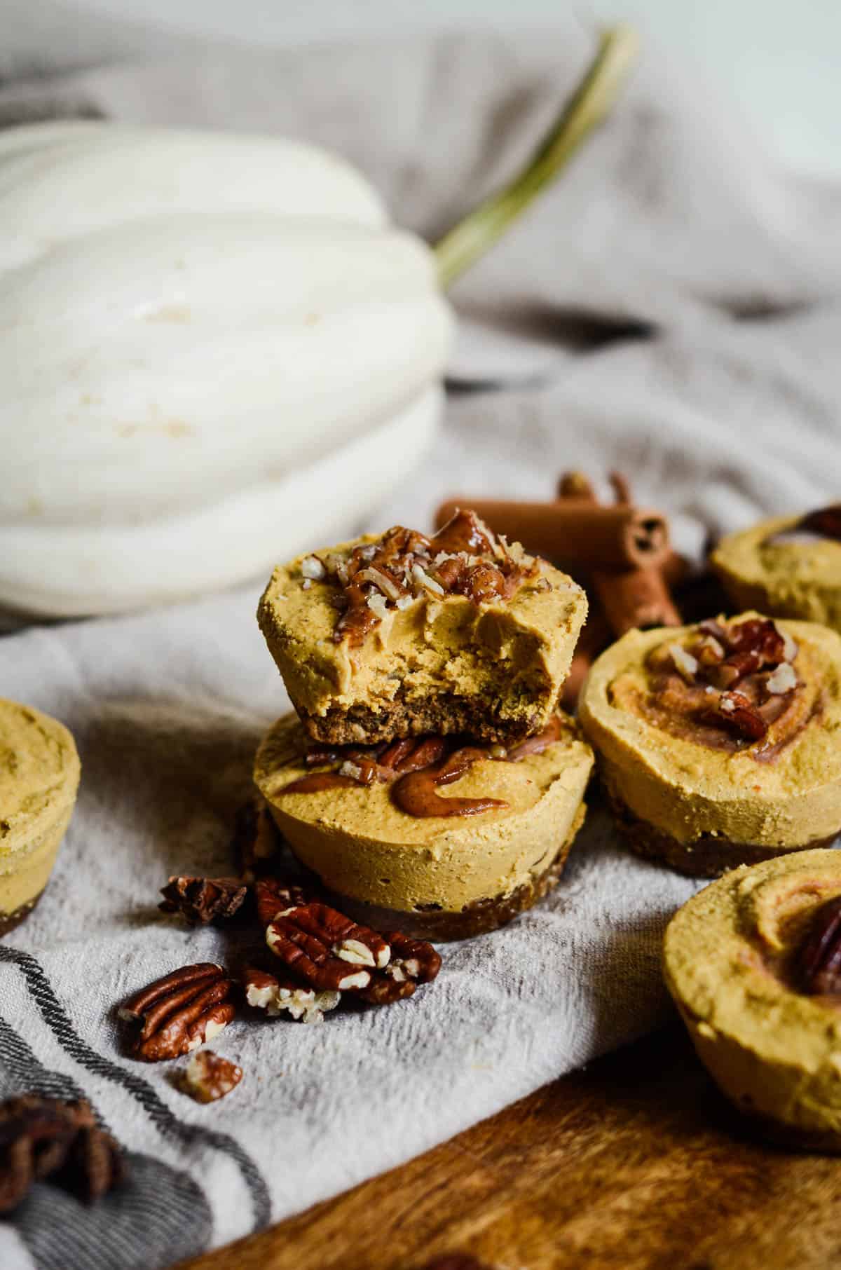 Little pumpkin colored cheesecakes with a dark brown gingersnap crust with a white pumpkin and pecans. 