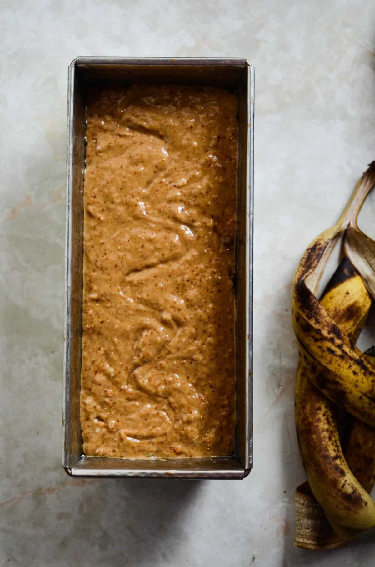 Banana bread wet batter in a rectangular pan ready to be baked, with banana peels beside it. 