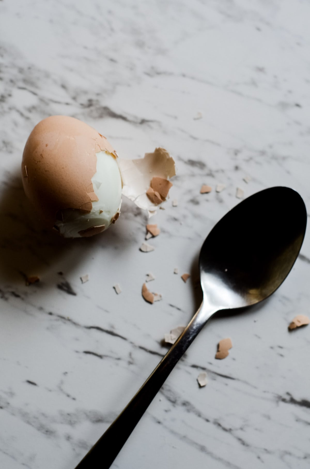 A boiled egg with the shell half off with a spoon beside it. 