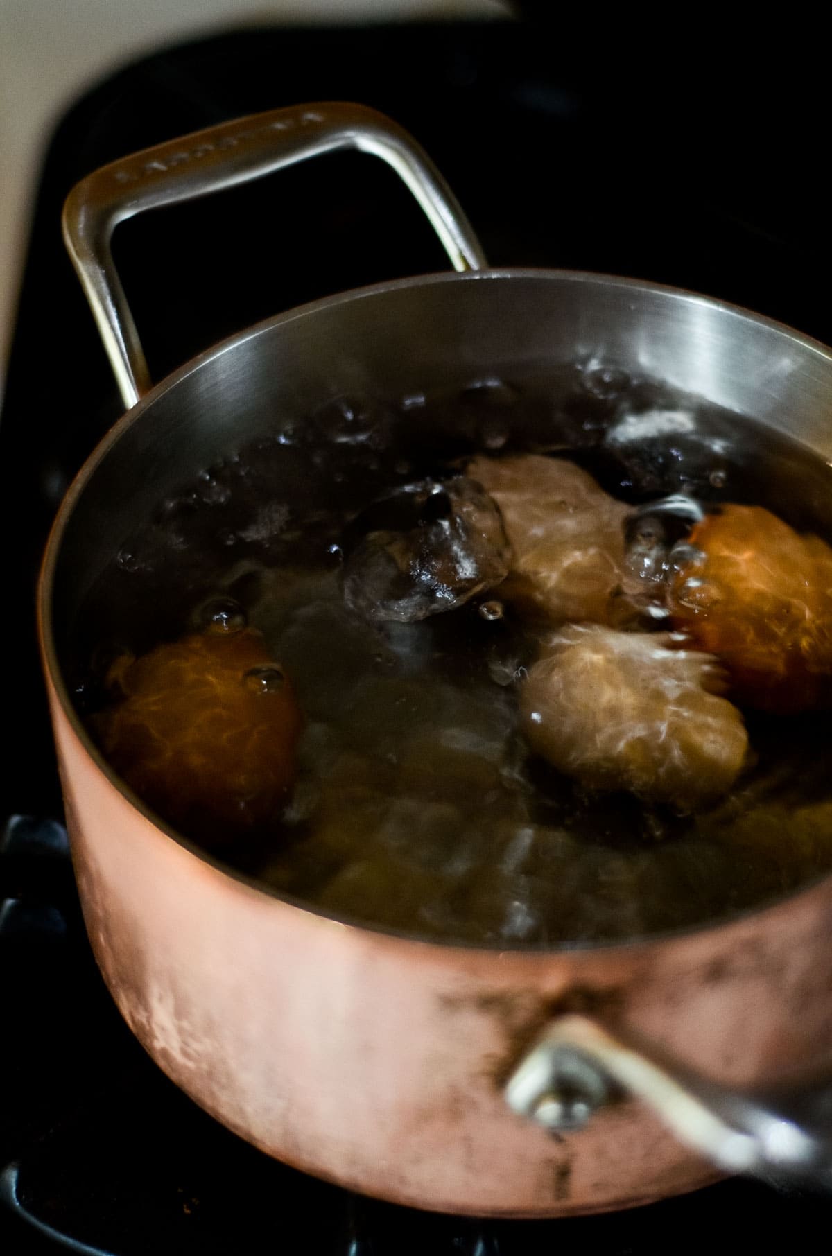 A pot on the stove with boiling water with eggs in the pot.