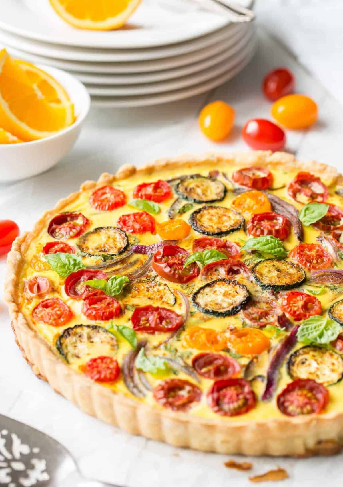 a pie crust with egg filling and bright colored tomatoes, onions, and zucchini on top.