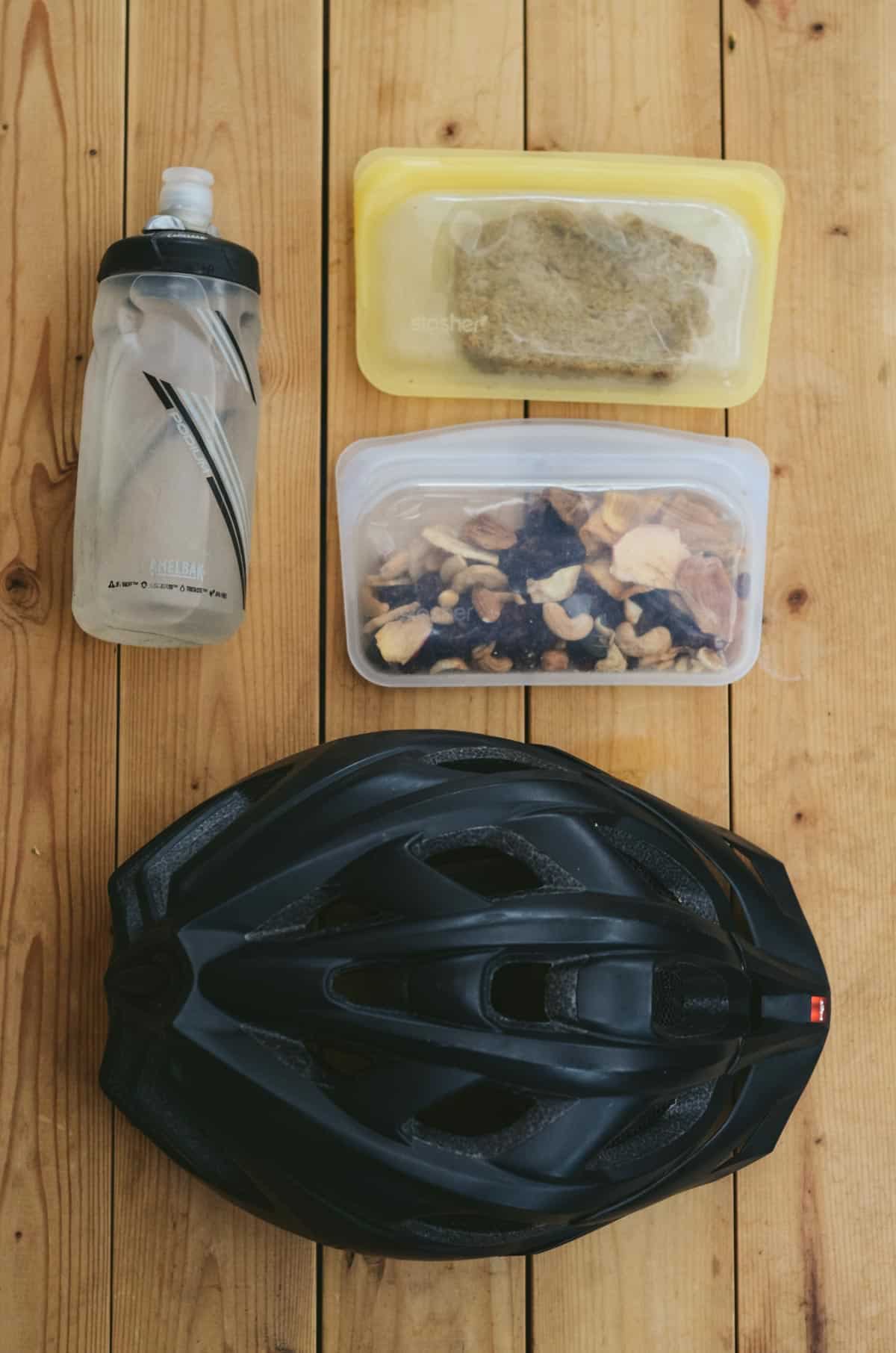 Bike helmet, water bottle, trail mix, homemade banana bread snack beside each other.