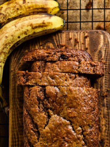 Thick slices of golden banana bread loaf on a cutting board beside bananas.