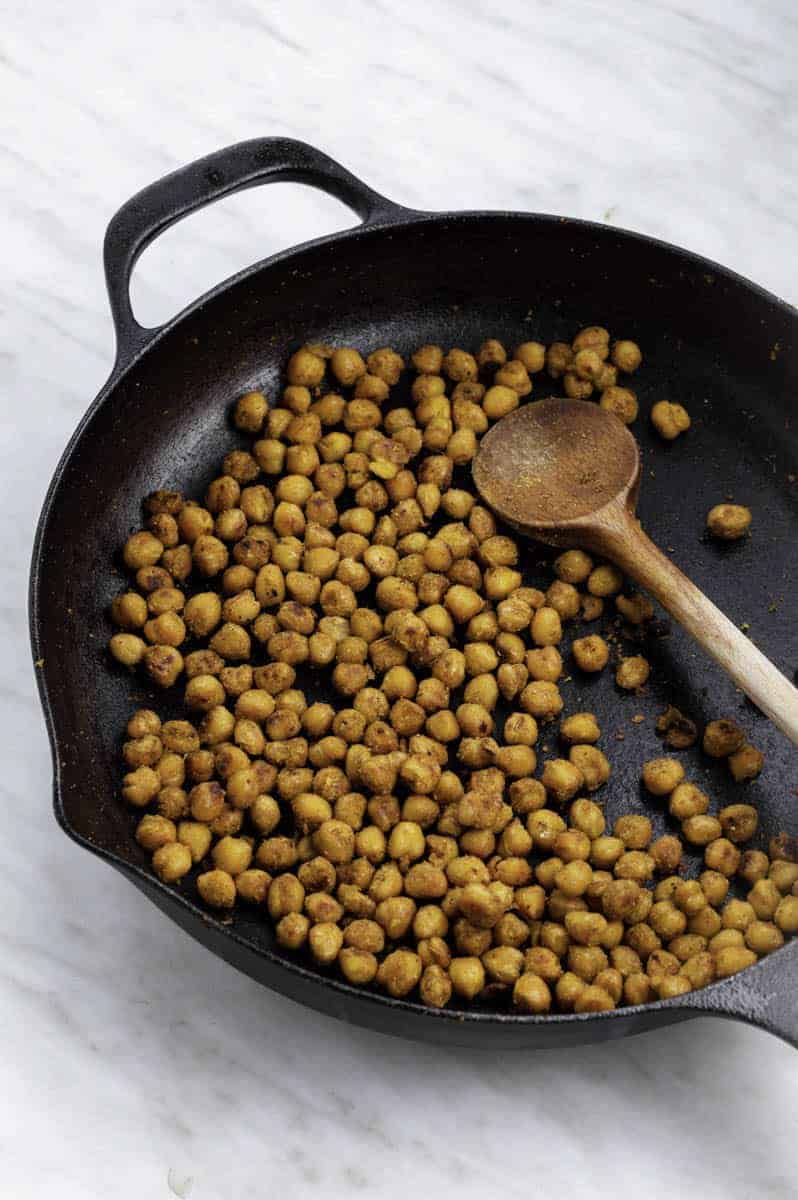 roasted chickpeas in a cast iron frying pan with a wooden spoon.