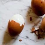 Three brown eggs on the counter with one half peeled.
