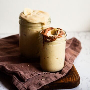 2 white banana smoothies on the counter, one with hemp hearts and almond butter on top.