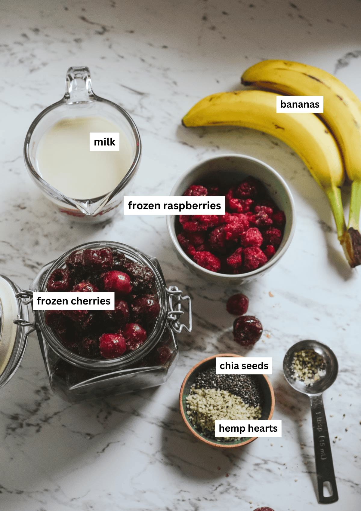 Ingredients for raspberry cherry smoothie in bowls: sweet dark cherries, frozen raspberries, almond milk, chia seeds, hemp hearts, and bananas.