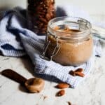 Homemade almond butter in a jar on the counter with almonds.