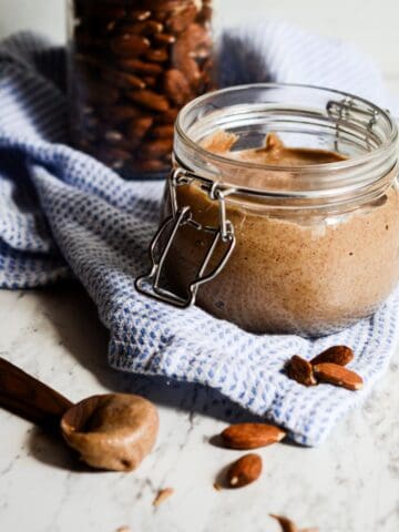 Homemade almond butter in a jar on the counter with almonds.