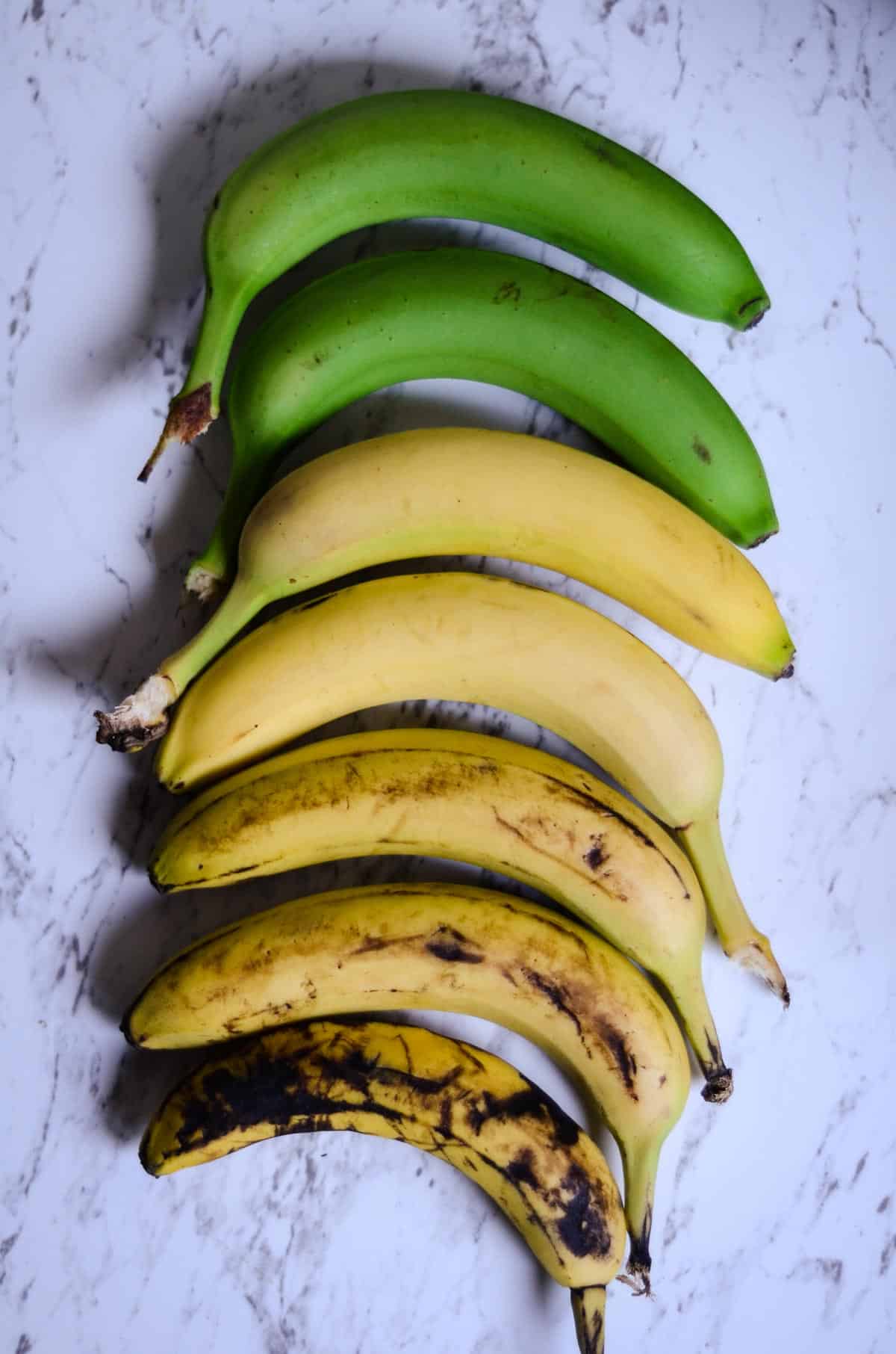 Green bananas, yellow bananas, and brown bananas laying on the counter.