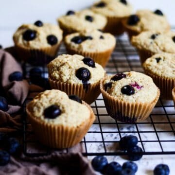 Muffins with big blueberries in them sitting on a cooling rack.