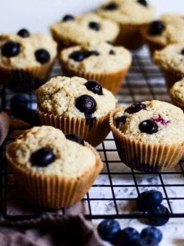 Muffins with big blueberries in them sitting on a cooling rack.