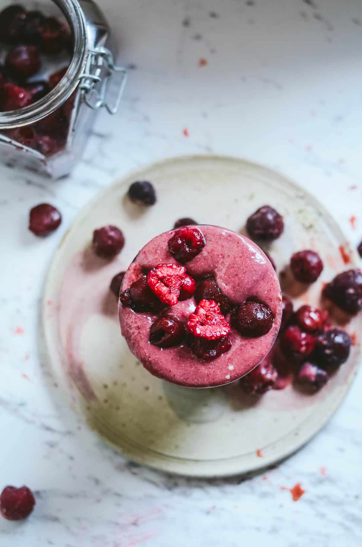 A dark red smoothie in a glass with frozen raspberries and cherries on top.